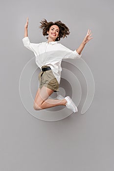 Full length image of positive girl 20s smiling and jumping, isolated over gray background