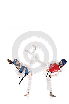 Full-length image of young competitive girls in dobok and helmet, practicing taekwondo, training isolated over white