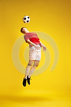 Full-length image of young man in uniform, soccer player, enthusiast in motion, training, hitting ball with head against