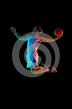 Full-length image of young men, basketball player in jump with ball, scoring goal against black background in neon light