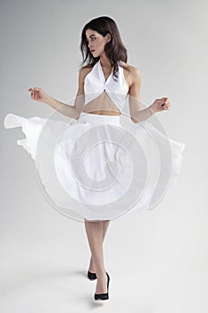 Full length image of young woman with hairstyle in white dress posing in studio, it spins, grey background.