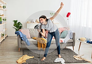 Full length of Indian teenage girl dancing and singing in messy room, using blowdryer as mic, having home concert