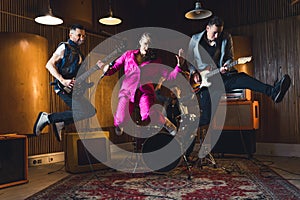 Full-length indoor shot of music band jumping. Lead singer and two guitarist jump in the air. Recording studio or garage