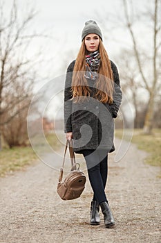 Full length lifestyle portrait of young and pretty adult woman with gorgeous long hair posing in city park with shallow depth of f