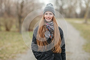 Full length lifestyle portrait of young and pretty adult woman with gorgeous long hair posing in city park with shallow depth of f