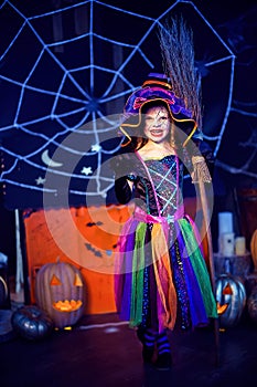 Full length of little girl in witch costume scaring, making faces with broom. Halloween party