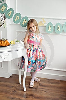 Full length of a little smiling girl in colorful dress posing in a decorated room for the holiday Easter is waiting for