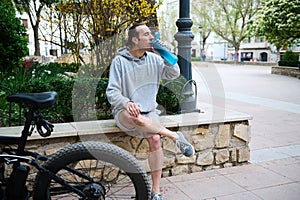 Full length male cyclist drinking water in the city. Electric motorbike, e-bike, electric bicycle bike on the foreground