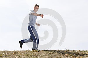 Full length of man checking time while jogging against sky