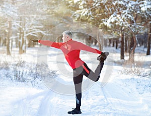 Full length of mature man in sportswear warming up before running outdoors on snowy winter day. Healthy lifestyle