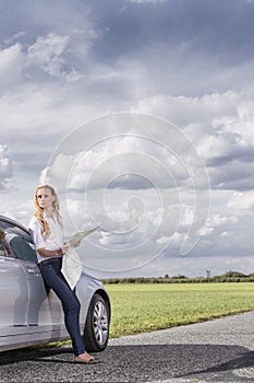 Full length of mid adult woman leaning on car while holding map at countryside