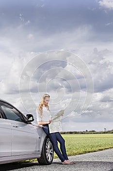 Full length of mid adult woman leaning on car while reading map at countryside