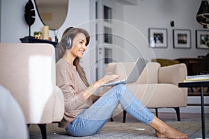 Full length of mid aged woman with headphone using a notebook at home