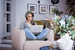 Full length of mid aged woman with headphone using a notebook at home