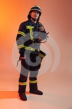 Full length. One male firefighter dressed in uniform posing over orange background in neon lights.