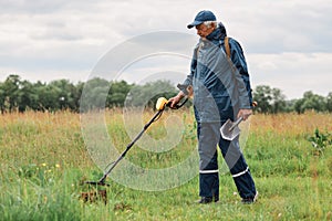 Full length outdoor portrait of numismatist in jacket and cap, holding in hands shovel and metal detector, looking for gold or