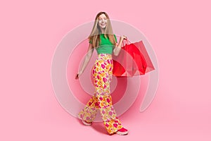 Full length photo of adorable cheerful girl dressed bright clothes carrying packages summer shopping isolated on pink