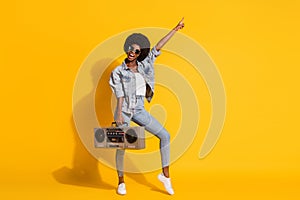 Full length photo of adorable lady wear casual denim outfit dancing boombox pointing empty space isolated yellow color