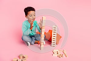 Full length photo of adorable little boy amazed play wooden cubes tall tower dressed stylish cyan garment isolated on