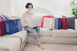 Full length photo of bob brunette haired woman sit sofa hold laptop buy sale bags inside home indoors