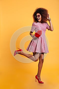 Full length photo of charming african retro stylish woman in dress and high heels standing on one leg while posing with big red l