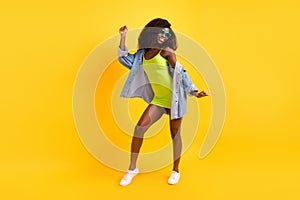 Full length photo of charming funky dark skin woman wear jeans shirt eyewear dancing isolated yellow color background