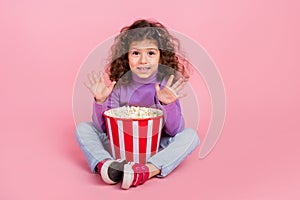 Full length photo of charming sweet little child dressed purple pullover waving arms hi eating pop corn isolated pink