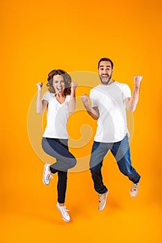 Full length photo of cheerful couple screaming in surprise while jumping, isolated over yellow background