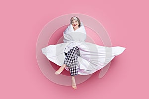 Full length photo of cheerful funny lady satisfied morning sitting bed hug warm blanket wear mask white plaid pajama