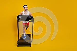 Full length photo of cheerful positive guy activewear running treadmill looking empty space isolated yellow color