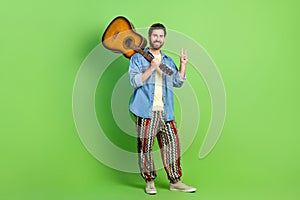 Full length photo of cheerful positive guy dressed jeans shirt enjoying guitar music showing v-sign isolated green color