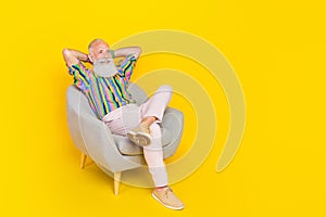 Full length photo of cheerful positive man sit chair arms behind head look empty space isolated on yellow color