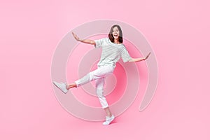 Full length photo of cheerful satisfied girl wear striped t-shirt white pants sneakers dancing have fun isolated on pink