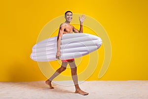 Full length photo of cool good mood shirtless man walking waving arm holding floating matrass  yellow color