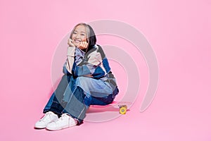 Full length photo of cute adorable youngster wear oversize sweatshirt sitting on skateboard in park isolated on pink