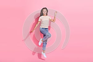 Full length photo of cute friendly girl dressed beige t-shirt jumping high waving hi arm isolated pink color background