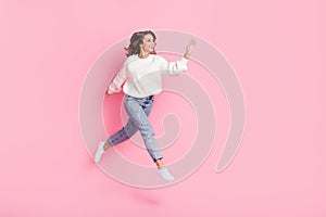 Full length photo of cute friendly woman dressed pullover waving arm empty space jumping high isolated pink color