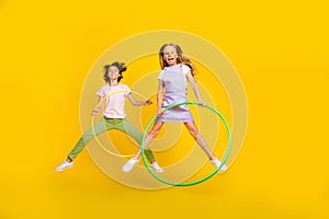 Full length photo of cute funky friends wear casual outfits jumping high playing hoola hoops isolated yellow color