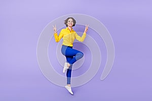 Full length photo of cute millennial brunette lady jump v-sign wear shirt pants sneakers isolated on purple background