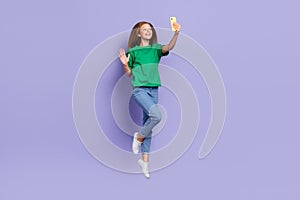 Full length photo of cute sweet girl dressed green t-shirt jumping high waving arm palm modern device isolated purple