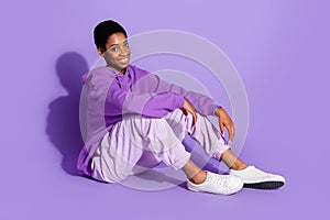 Full length photo of cute young guy sit wear hoodie trousers footwear isolated on violet color background