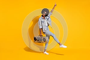 Full length photo of cute young woman wear casual jeans clothes holding boombox pointing empty space isolated yellow