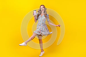 Full length photo of dreamy excited woman dressed flower print sarafan drinking cacao having fun isolated yellow color