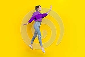 Full length photo of dreamy excited woman dressed purple shirt jumping waving arm empty space isolated yellow color