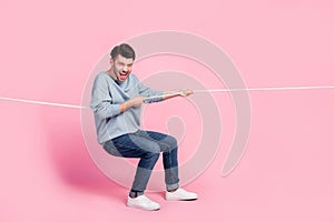 Full length photo of excited guy competitor pulling tug war string isolated on pastel color background