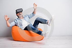 Full length photo of excited man sit chair happy have fun wear virtual reality glasses play game isolated over grey
