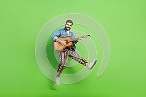 Full length photo of excited positive guy dressed jeans shirt jumping high enjoying guitar music isolated green color