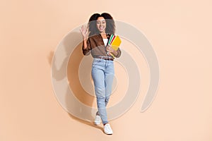 Full length photo of friendly positive girl wear brown blouse holding copybook waving palm say hi isolated on pastel