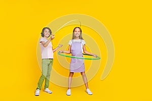 Full length photo of funky cheerful friends wear casual outfits playing hoola hoops isolated yellow color background