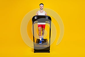 Full length photo of funky cheerful guy activewear walking treadmill empty space isolated yellow color background